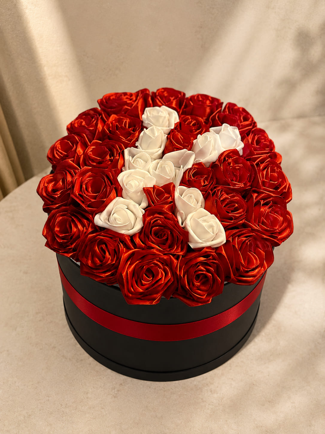 Round black box of red roses with a white rose K initial, personalised flower gift delivery in Fes